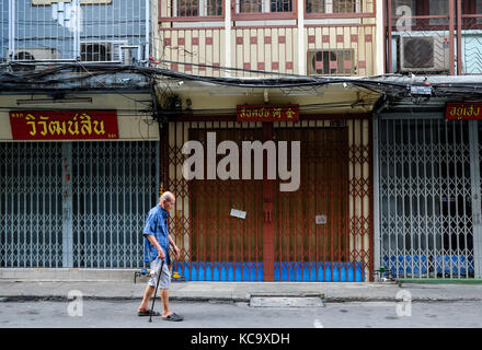 Un anziano uomo tailandese cammina giù per una strada nell'area di Chinatown di Bangkok, Thailandia Foto Stock