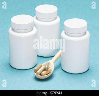 Cucchiaio di legno le capsule riempite e vasi di colore bianco su sfondo blu Foto Stock