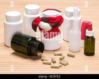 Il trattamento di raffreddori e influenza. vaso di pillole, legato con sciarpa lavorata a maglia, vasi di medicinali, sparse in capsule, inalatore, spray nasale e gocce con pipetta Foto Stock