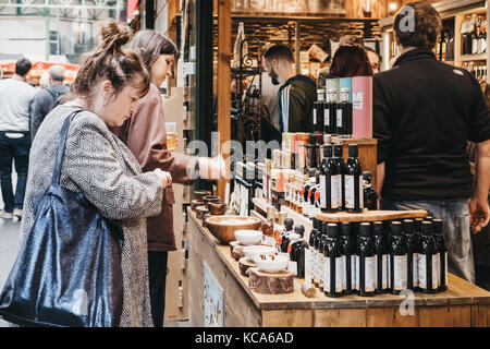 Donne provano l'olio d'oliva e aceto in un mercato in stallo nel mercato di Borough, uno dei più grandi e più antiche i mercati alimentari a Londra. Foto Stock