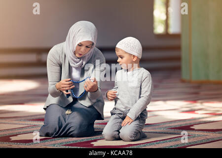 Mamma musulmana insegnare a suo figlio di pregare all'interno della moschea Foto Stock