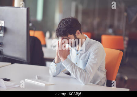 Azienda giovane uomo che lavora sul computer desktop al suo banco nel moderno luminoso ufficio di avvio interno Foto Stock