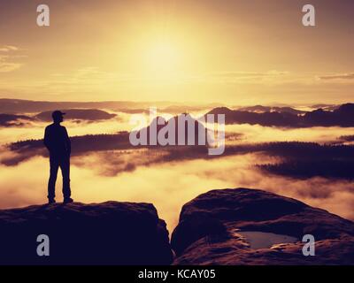 Tall escursionista in nero gustano orange sunrise sul punto di vista. pesanti soffietto di nebbia in valle. splendida alba in montagna. Foto Stock