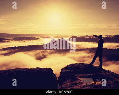 Tall escursionista in nero gustano orange sunrise sul punto di vista. pesanti soffietto di nebbia in valle. splendida alba in montagna. Foto Stock