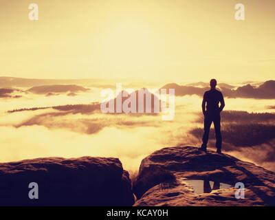 Tall escursionista in nero gustano orange sunrise sul punto di vista. pesanti soffietto di nebbia in valle. splendida alba in montagna. Foto Stock