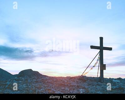 Grande croce sulla cima della montagna come tipico delle Alpi. croce di legno al picco di montagna con la preghiera buddista flags flutter in forte vento. Monumento a vi Foto Stock