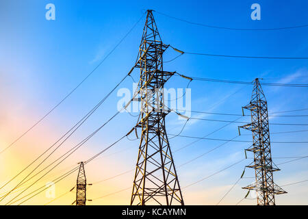 Di energia elettrica ad alta tensione e tralicci di trasmissione delle linee di alimentazione sul cielo blu sullo sfondo. Foto Stock