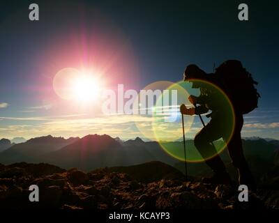 Lens Flare leggero, forte difetto. silhouette di un uomo con il cofano,zaino e pali in mano. l'uomo cammina sul picco roccioso di montagna. giornata di sole montagne rocciose Foto Stock