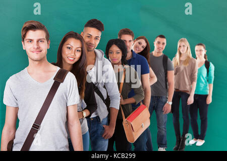 Gruppo di multi-etnico studente di college in piedi in fila contro lo sfondo di colore verde Foto Stock