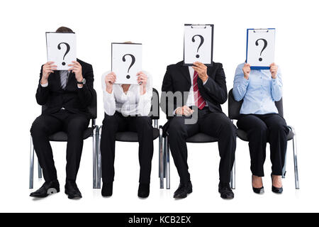 Gli imprenditori nascondendo loro faccia dietro un punto interrogativo segno su sfondo bianco Foto Stock