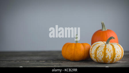 Tre zucche arancione scuro sul tavolo di legno su uno sfondo grigio, concetto di halloween Foto Stock