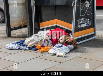 Traversina ruvida / persona senzatetto, leggendo una rivista accanto a un Evening Standard edicola, sdraiato sul pavimento a Londra, Inghilterra, Regno Unito. Foto Stock