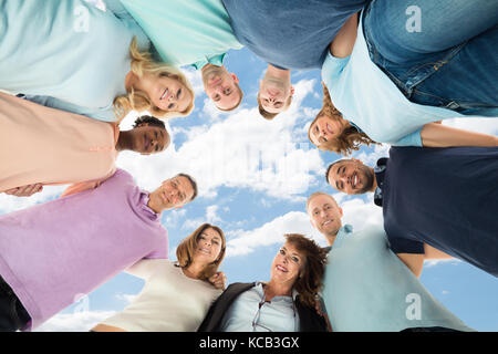Ritratto di un felice multietnica formando amici Huddle contro Sky Foto Stock