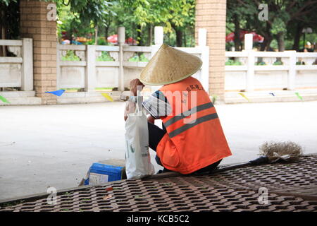 Lavoratore con riso hat seduto su un marciapiede Foto Stock