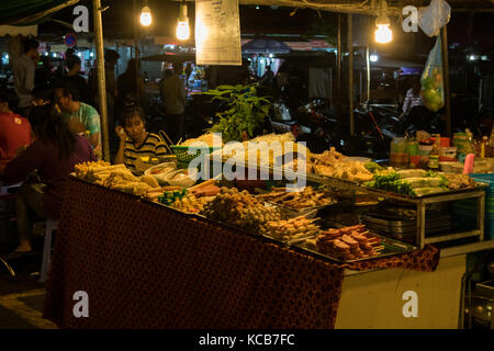 Un cibo asiatico fornitore, la vendita di cibo di strada a Phnom Penh il mercato notturno, in Cambogia. Il cibo è principalmente fritti e a buon mercato e di sperimentare la cucina asiatica. Foto Stock