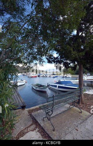 Il bellissimo porto di San Stefanos sull'isola greca di Corfù. Un banco vuoto sul lato di un pittoresco porto su un isola in Grecia. Foto Stock