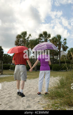 Caucasian Senior Couple (60-70 anni) tenendo ombrelloni mentre camminando giù pathway, Myrtle Beach SC, USA. Foto Stock