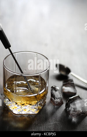 Whisky in un bicchiere e pezzi di ghiaccio su un legno Foto Stock