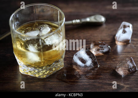 Whisky in un bicchiere e pezzi di ghiaccio su un legno Foto Stock