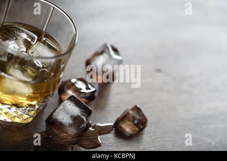 Whisky in un bicchiere e pezzi di ghiaccio su un legno Foto Stock