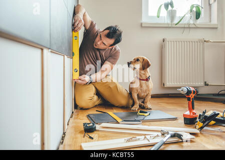 L'uomo facendo lavori di ristrutturazione a casa insieme con il suo piccolo cane giallo Foto Stock