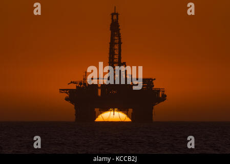 Il sole tramonta dietro un olio piattaforma di trivellazione ancorato nell'Oceano Atlantico a longbeach nel deserto del Namib di Namibia Foto Stock