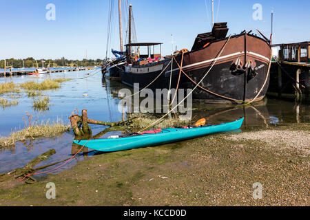 Un turchese canoa legata sul fango sul pin mill accanto a chiatte ormeggiate, curve di scafi e funi di ormeggio, Chelmondiston, Essex, Regno Unito Foto Stock