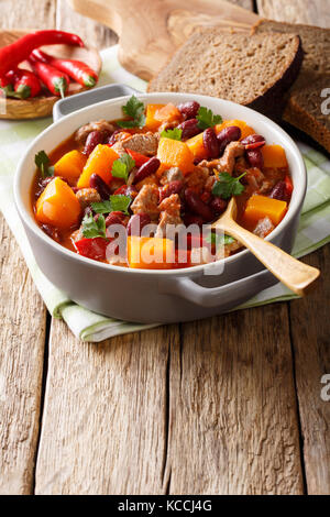 Spezzatino di manzo, zucca, fagioli rossi, i pomodori e il peperoncino close-up in una pentola sul piano verticale. Foto Stock