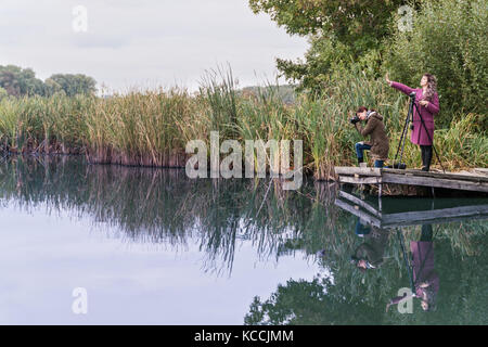 Due donne di fotografare un paesaggio in piedi su un molo sulle acque del lago nella foresta Foto Stock