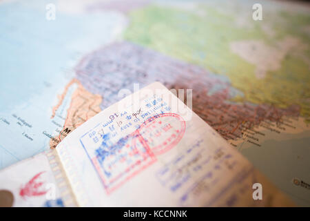 (Fuoco selettivo) un passaporto con francobolli è su un sfocata mappa geografica del mondo. Il passaporto mostra alcuni timbri di ingresso in vari paesi arou Foto Stock
