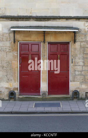 Due rosso scuro porte anteriori sul muro di pietra, street pavimentazione con raschiatori di avvio Foto Stock