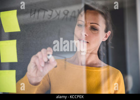 La donna la scrittura di note sulla scheda di vetro presso l'ufficio Foto Stock