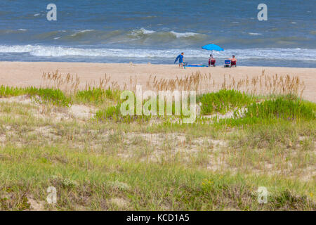 Avon, Outer Banks, North Carolina, Stati Uniti d'America. La vegetazione si stabilizza un isola barriera mentre due Aduits e un giovane ragazzo rilassarsi sull'Oceano Atlantico Beach. Foto Stock