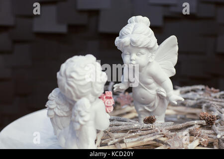Due statue di angeli con le ali e una corona di ramoscelli su uno sfondo scuro per natale Foto Stock