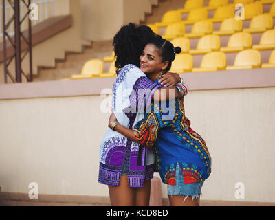 Due belle felice afro-americane donne amici abbraccia ogni altra outdoor. giovani razza mista le ragazze che indossano vestiti colorati comunica, gode la riunione e il messaggio di saluto Foto Stock