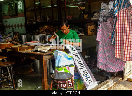 Uomo tailandese rendendo insegne di un piccolo negozio a Bangkok, in Thailandia Foto Stock