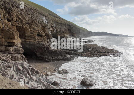 Le ripide rocce di ogmore mostra una piccola grotta ingresso nelle alte rocce della costa con una bassa marea e piccole onde. Foto Stock