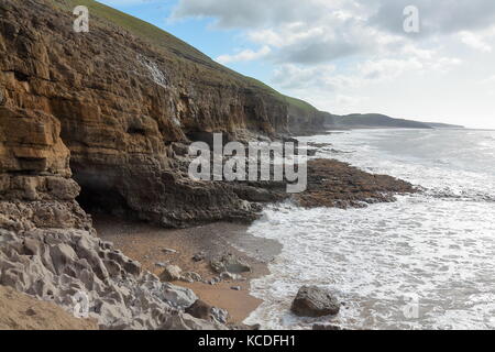 Le ripide rocce di ogmore mostra una piccola grotta ingresso nelle alte rocce della costa con una bassa marea e piccole onde. Foto Stock