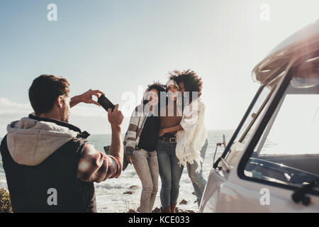 Amici su roadtrip con uomo a scattare foto di donne all'esterno. Donna sorridente fotografata da maschio. Foto Stock