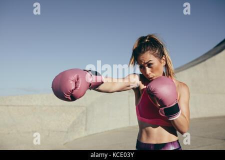 donna sportiva che indossa guanti da boxe per allenarsi all'aperto. Pugile femminile che pratica pugilato. Foto Stock