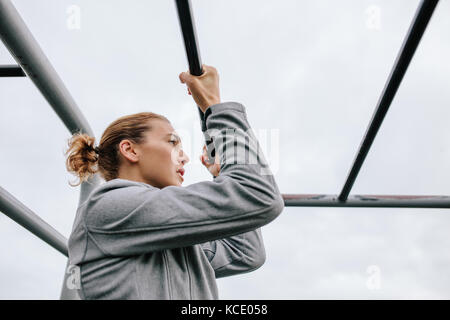 Atletica Giovane donna facendo esercizi outdoor su attrezzature fitness. Montare donna climbing Monkey bar durante la corsa a ostacoli in allenamento di fitness. Foto Stock