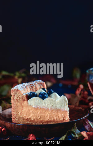 Crosta hommemade torta con crema wipped, mirtilli e purea di zucca su sfondo scuro con tazzina, foglie di autunno e cannella. close-up di un pezzo di torta. autunno ancora vita con prodotti di pasticceria. Foto Stock