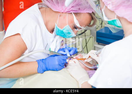 Una giovane donna dentista in bianco uniforme medica e il suo assistente sono il trattamento di denti dalla carie e denti di compensazione da placca in un moderno denta Foto Stock