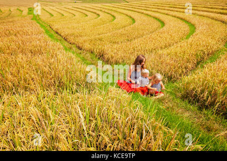 Felice figlia della madre, baby figlio a piedi con il divertimento in terrazza plantation con riso crescente. splendida vista dei campi tradizionali. Viaggi avventura con ch Foto Stock