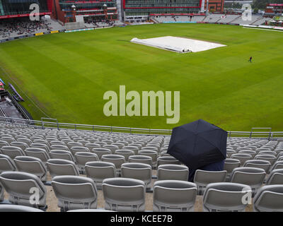 Persona seduta sotto la pioggia a una partita di cricket Foto Stock