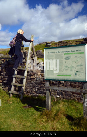 Donna escursionista arrampicata scaletta in legno stile presso il vecchio dismesse miniere di piombo su grassington moor, wharfedale, Yorkshire Dales National Park, Inghilterra, Regno Unito. Foto Stock