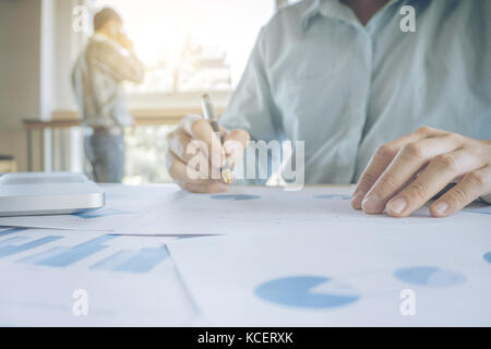 Bel giovane imprenditore lavora con il computer portatile mentre è seduto sulla scrivania in ufficio e statistica finanziaria grafico. Foto Stock