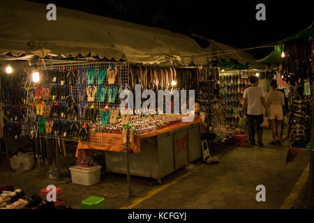 Uno stallo a Phnom Penh il mercato notturno, la vendita di accessori vari quali cinghie, flip-flop e orologi. In attesa per i clienti. Cambogia, SE Asia Foto Stock