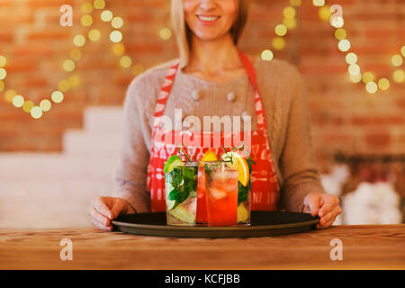 Giovane donna graziosa con il rosso e il verde cocktail sul vassoio in bar Foto Stock