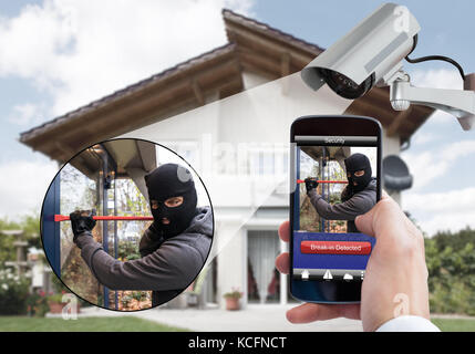 La persona tenuta a mano mobile phone rilevare ladro nel sistema di sicurezza con telecamere di sorveglianza dietro Foto Stock